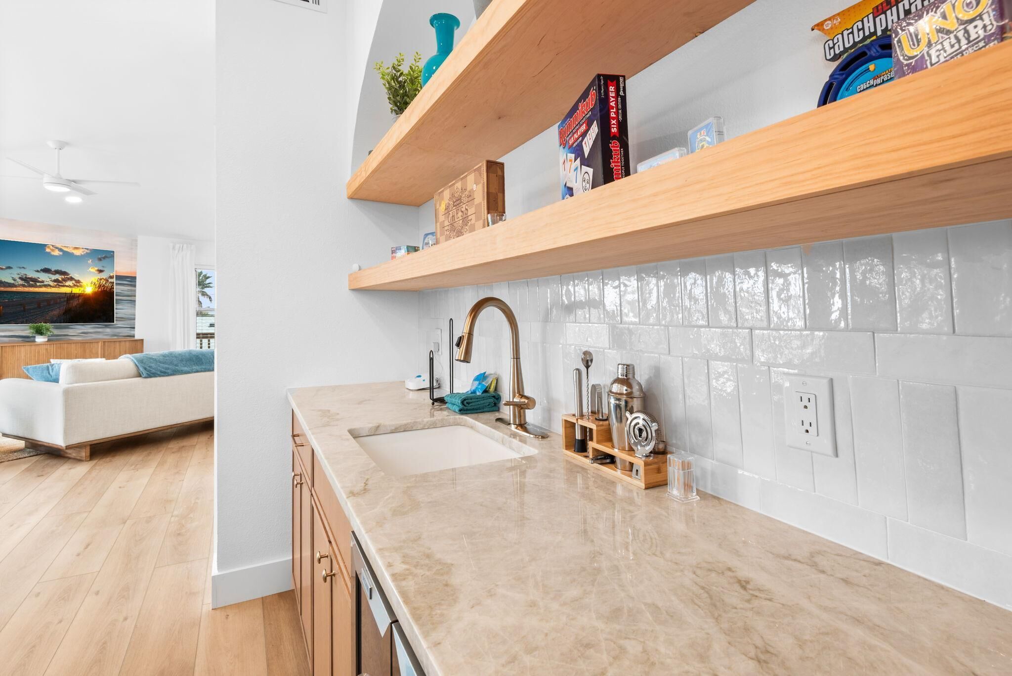A modern kitchen with a marble countertop, wooden shelves, and a view of the living area.