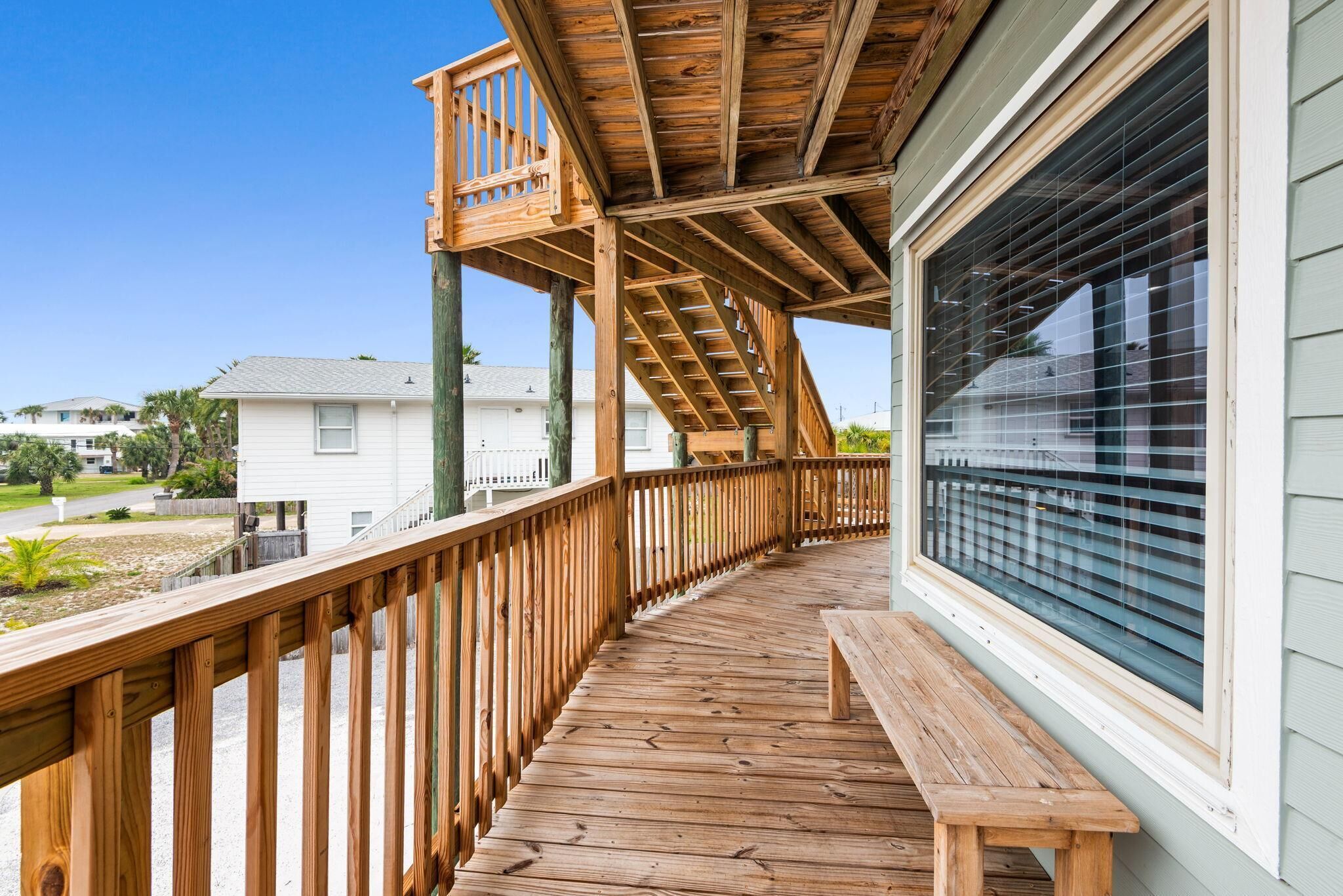 A wooden deck with a bench, a staircase, and a window with blinds.