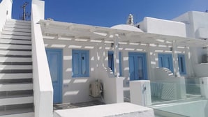 Edifici blanc amb portes i finestres blaves, una escala i una barana de vidre.