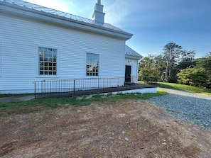 A white building with a porch and a gravel driveway.