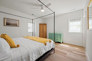 A bedroom with a four-poster bed, a ceiling fan, a wooden wardrobe, and a green dresser.