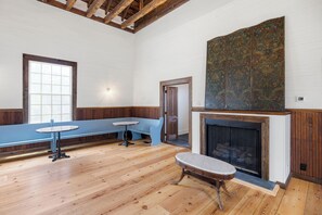 A room with a wooden floor, a bench, a table, a fireplace, and a large decorative panel.