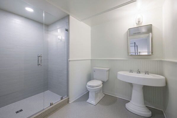 A bathroom with a walk-in shower, toilet, and pedestal sink.