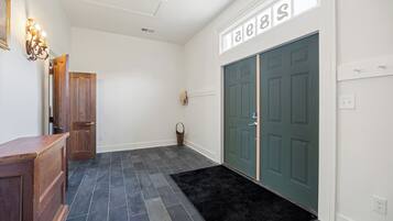 Un couloir avec une porte en bois, un tapis noir et un luminaire fixé au mur.