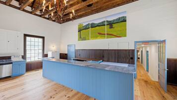 Une cuisine moderne dotée d’un îlot central, de poutres en bois au plafond et d’un grand tableau représentant un paysage accroché au mur.