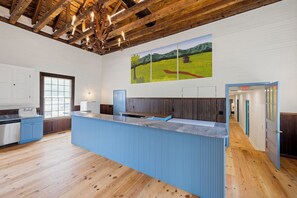 A modern kitchen with a central island, wooden beams on the ceiling, and a large landscape painting on the wall. - Historic Church Turned Home in Charlottesville (Scottsville)