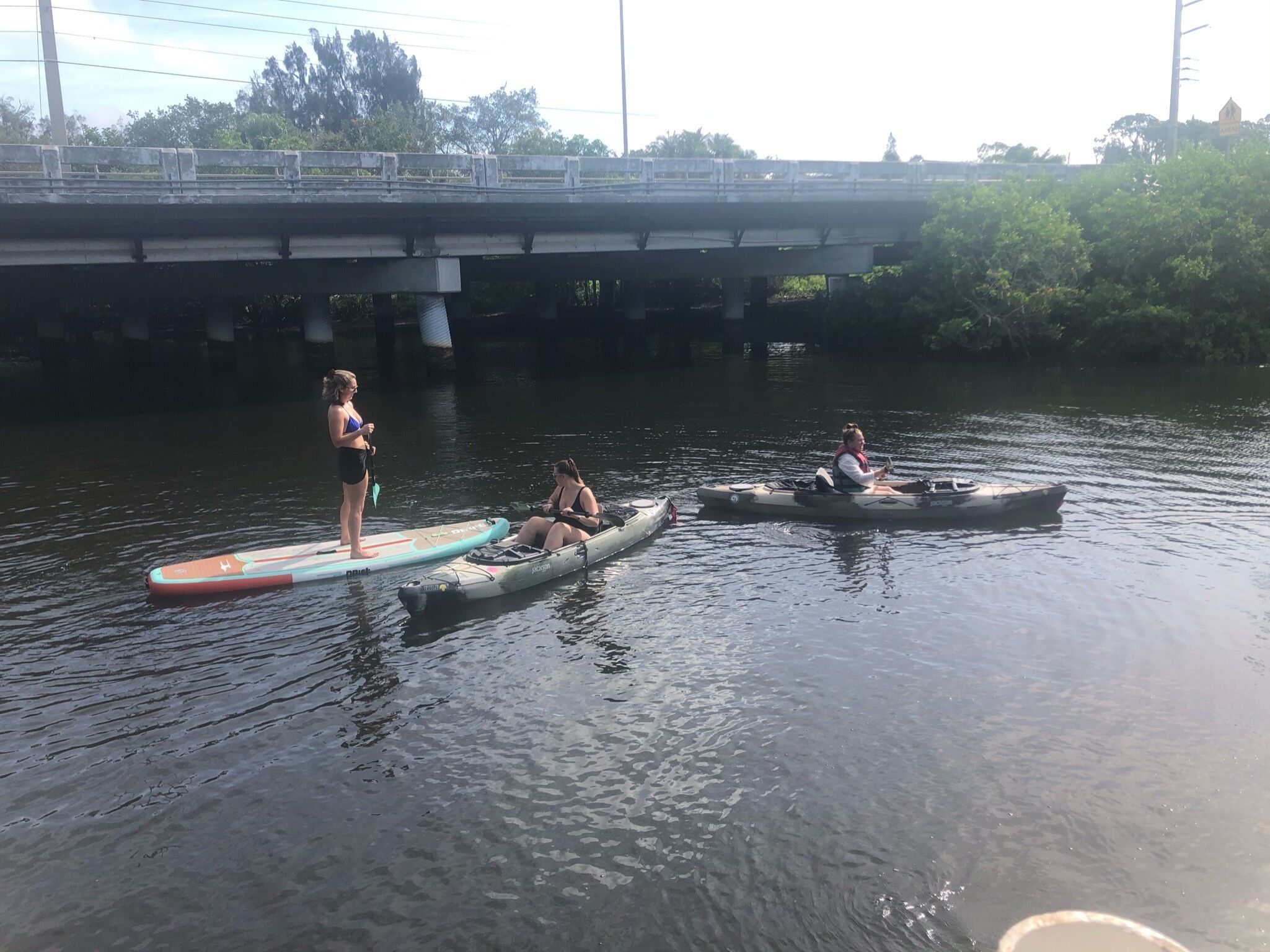 Escena de río con tres personas en tablas de remo y kayaks.