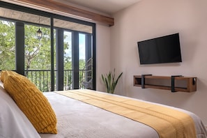 Ein Schlafzimmer mit Bett, einem an der Wand befestigten Fernseher und einem Balkon mit Blick auf Bäume.