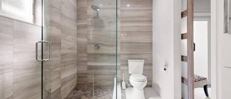 A modern bathroom with a glass-enclosed shower, a toilet, and a wooden door.