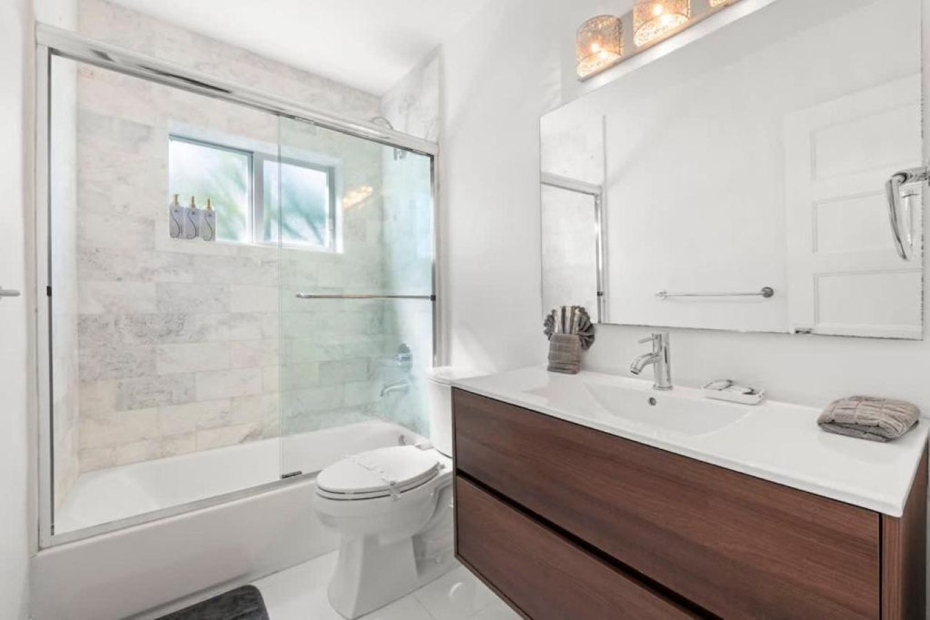 A modern bathroom with a glass-enclosed shower, a white toilet, a large mirror, and a vanity with a sink and towel.