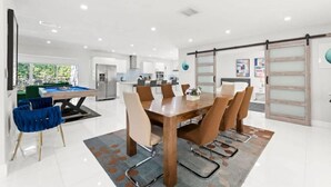 A modern kitchen with a dining area, a pool table, and a view of the outdoors. - Casa Oasis by Glam Homes (Ojus)