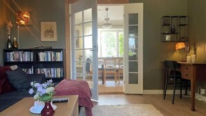 A living room with a sofa, a coffee table with a vase, a bookshelf, a desk, and a door leading to a dining area. - Charming villa by the sea - sandy beach and sea view in Gislövs Location (Trell)