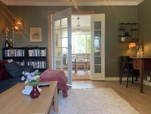 A living room with a sofa, a coffee table with a vase, a bookshelf, a desk, and a door leading to a dining area. - Charming villa by the sea - sandy beach and sea view in Gislövs Location (Trell)