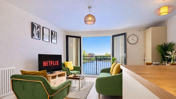 Una sala de estar moderna con televisor, sofás verdes, una mesa de centro de madera y vistas a un cuerpo de agua.