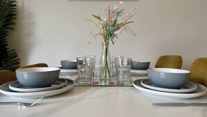 Una mesa de comedor lista con fuentes, vasos y un jarrón de flores.