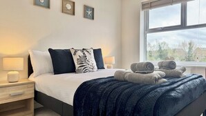 Una cama bien hecha con almohadas, una lámpara de noche y una ventana con vistas al exterior.