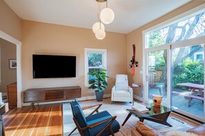 A modern living room with a flat-screen TV, a potted plant, a white chair, and a glass coffee table. - Casa Soleil: Luxurious Cottage Steps Away from Downtown Ashland (Ashland)