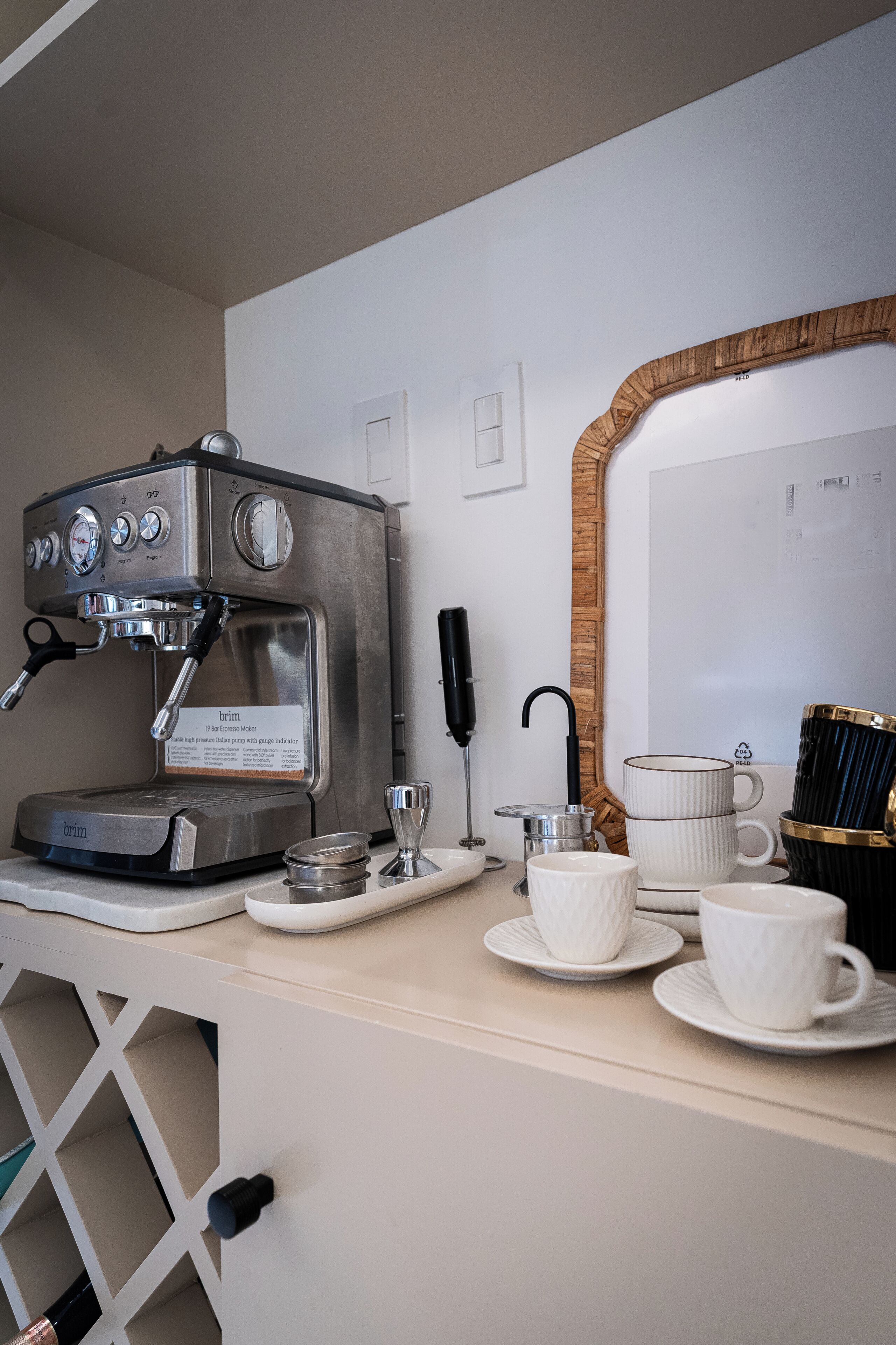 Una cafetera, un espejo y una bandeja con tazas y una jarra de café sobre una encimera.