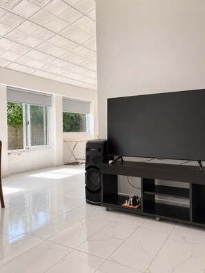 A spacious room with a large flat-screen TV on a black stand, a large speaker, and a chessboard on the stand.