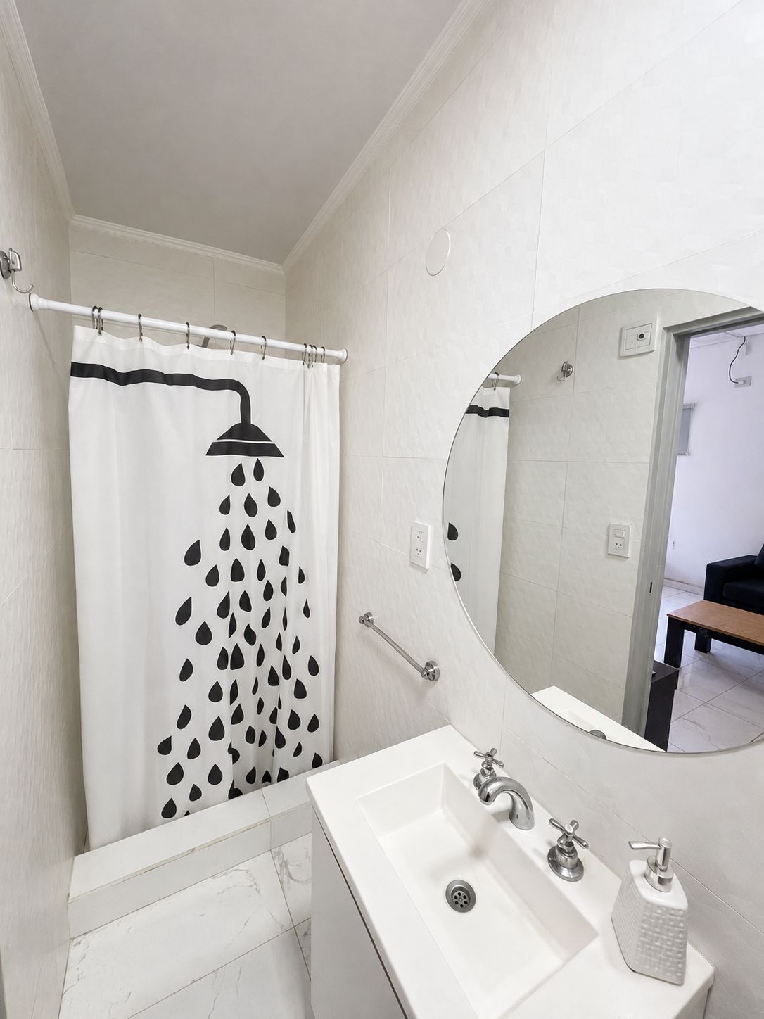 Un baño con cortina de ducha con diseño de lluvia, un lavabo blanco con dispensador de jabón y un espejo con marco redondo.