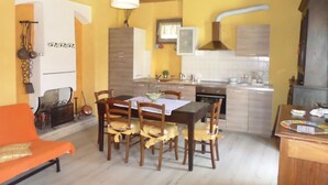 A dining area with a wooden table and chairs, a kitchen with modern appliances, and a yellow wall.