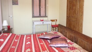 A bedroom with a bed, a desk, a chair, a window with curtains, and a wooden wardrobe.