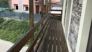 A wooden balcony with a view of a pink building and a stone wall.