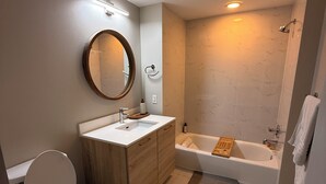 Et moderne badeværelse med toilet, vask, spejl og badekar.