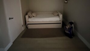 Et lille rum med en hvid sofa, en dør, et billede i ramme på væggen og en taske på gulvet.
