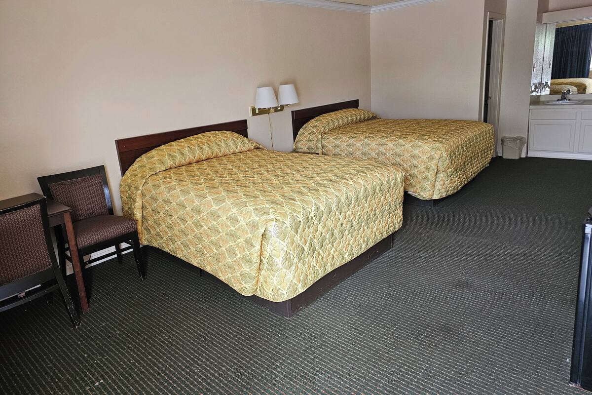 Habitación de hotel con dos camas, una silla, un escritorio y una kitchenette pequeña.