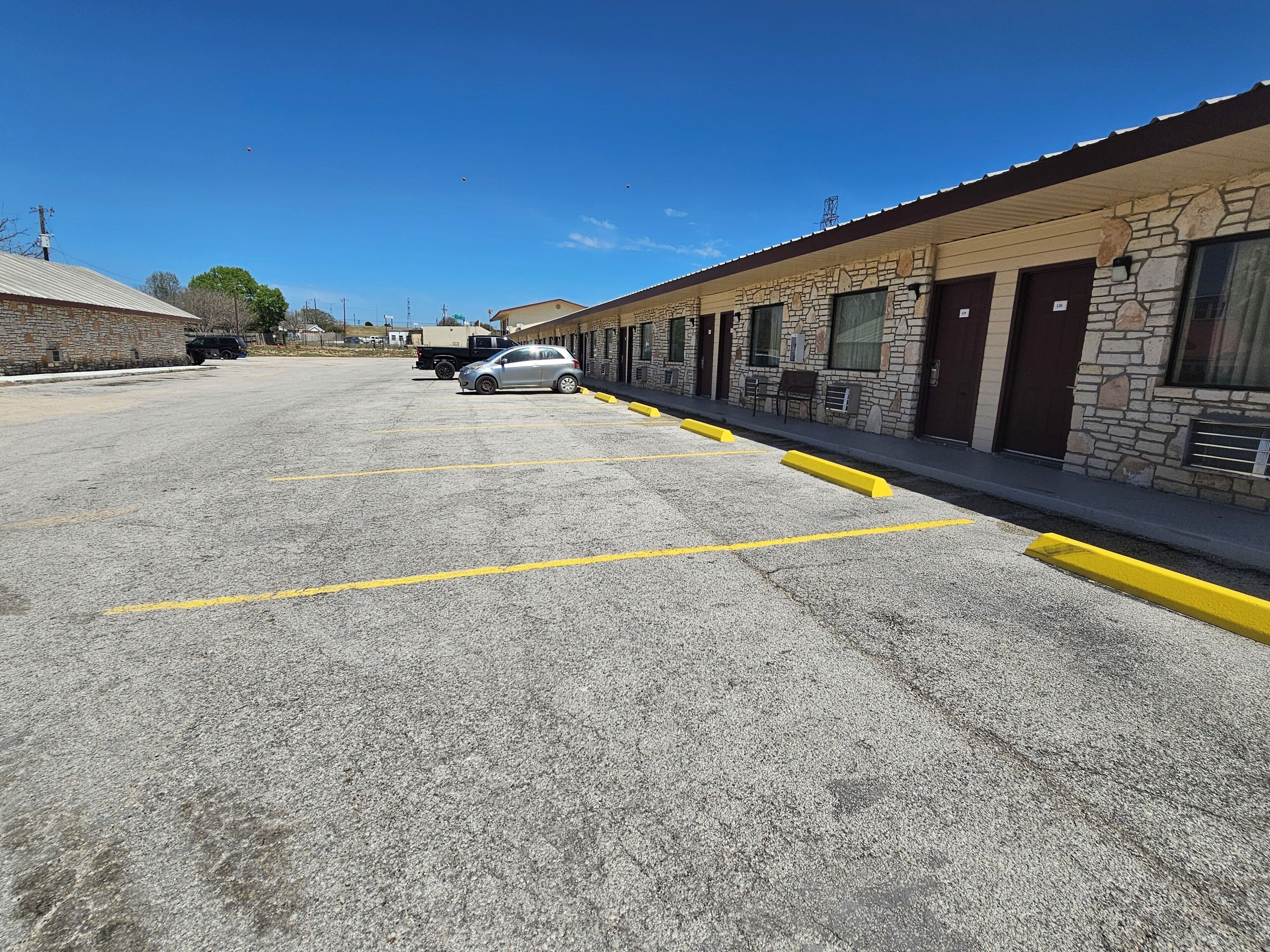 A parking lot with marked spaces, a row of stone buildings with large windows, and a clear blue sky.