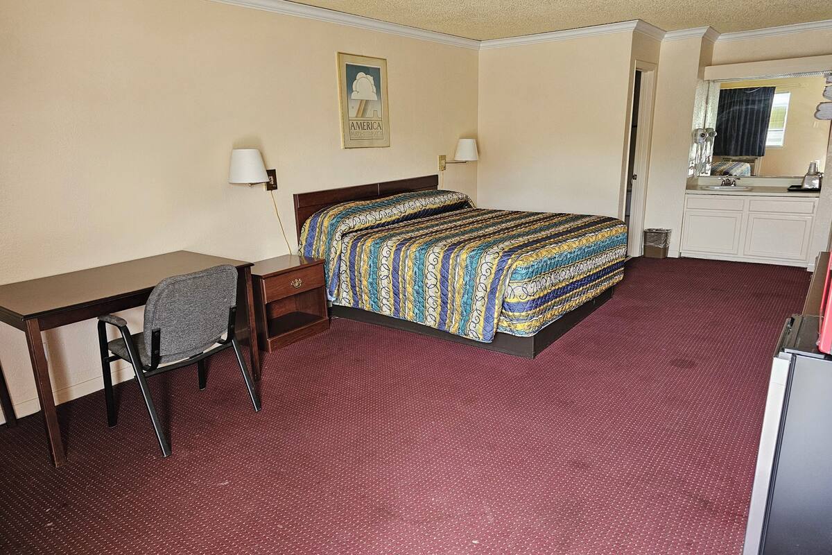 Habitación de hotel con cama, escritorio, silla y una kitchenette pequeña.