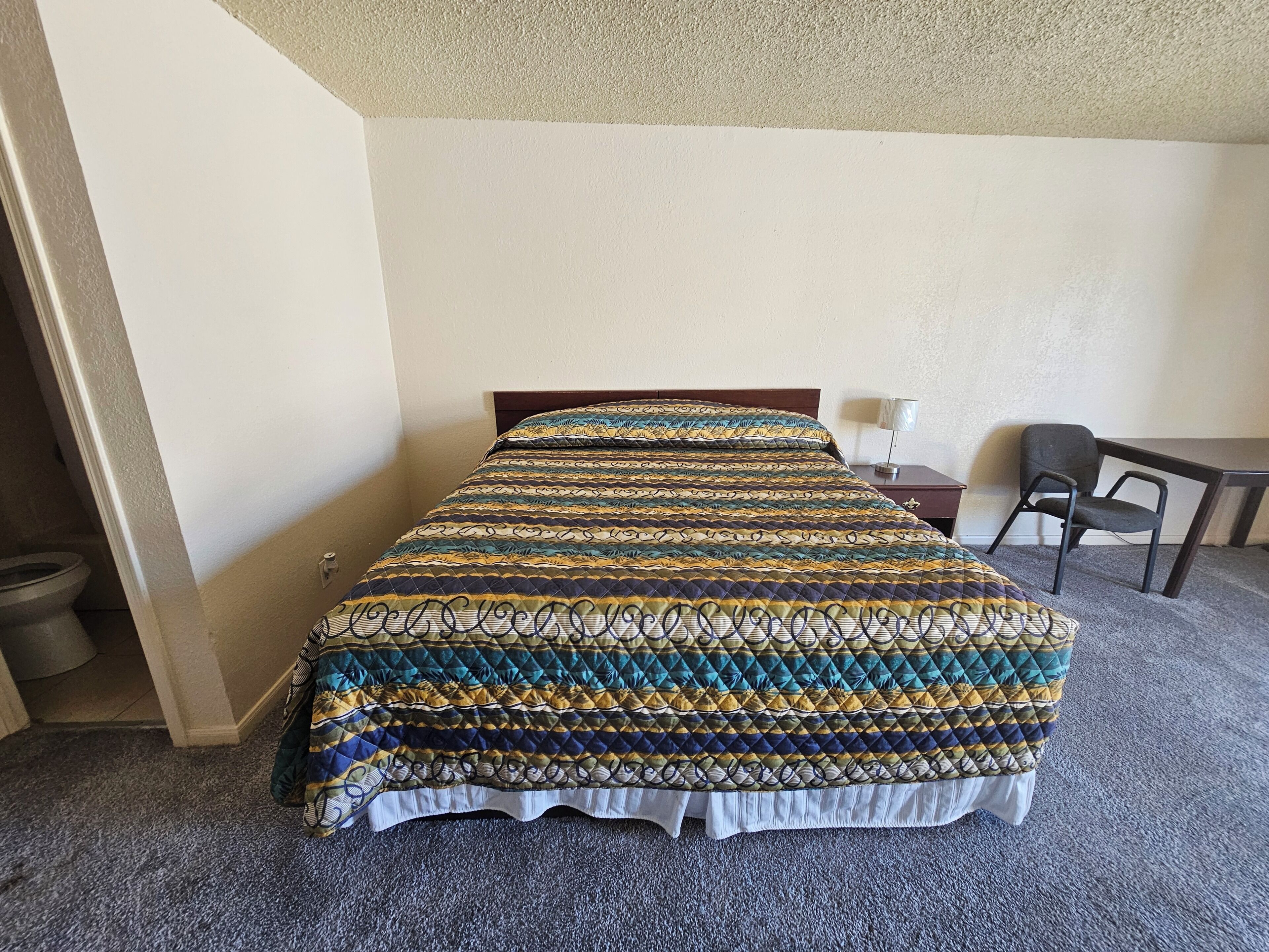 Une chambre d’hôtel avec un lit, un bureau, une chaise et des toilettes.