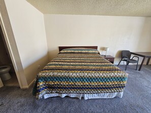 Una habitación de hotel con cama, escritorio, silla y un inodoro.