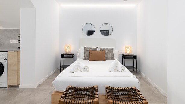 Una habitación de hotel moderna con una cama bien hecha, dos lámparas de noche, una lavadora y una pequeña zona de estar.