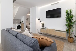 A modern living room with a grey sofa, a flat-screen TV, a potted plant, and a kitchen in the background. - Cabanyal Station A. WiFi + 3 Pax (Valencia / València)