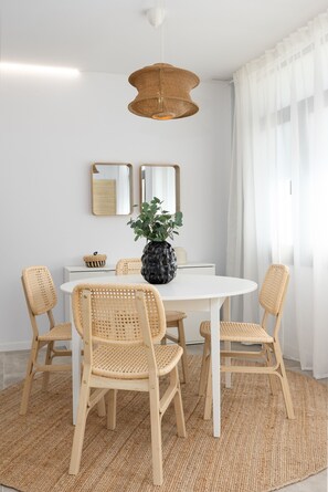 A dining area with a round white table, four wicker chairs, a central potted plant, a hanging woven light fixture, and two wall-mounted mirrors. - Cabanyal Station A. WiFi + 3 Pax (Valencia / València)