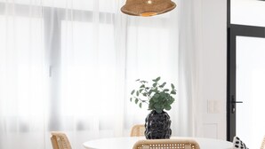 Un comedor con una mesa redonda, sillas de mimbre, una lámpara colgante y una planta en maceta.