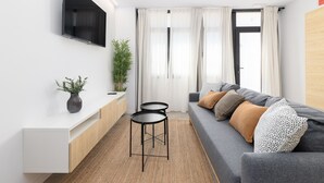 Ein modernes Wohnzimmer mit einer Couch, zwei Beistelltischen, einem Flachbildfernseher und einer Topfpflanze.