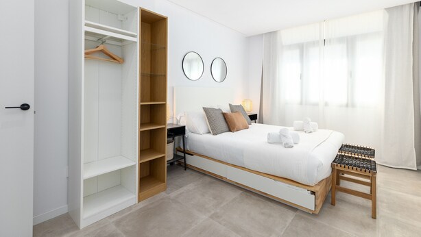 Ein Schlafzimmer mit einem Bett, einem Kleiderschrank, einem Schreibtisch und einem Fenster mit Vorhängen.