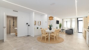 Eine moderne Küche mit weißen Schränken, ein Essbereich mit rundem Tisch und Stühlen sowie ein graues Sofa.