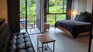 A modern bedroom with a large bed, a sofa, a small table, and a balcony with a view of a garden. - Naki Apartamento Santa Rosa de Cabal (Santa Rosa de Cabal)