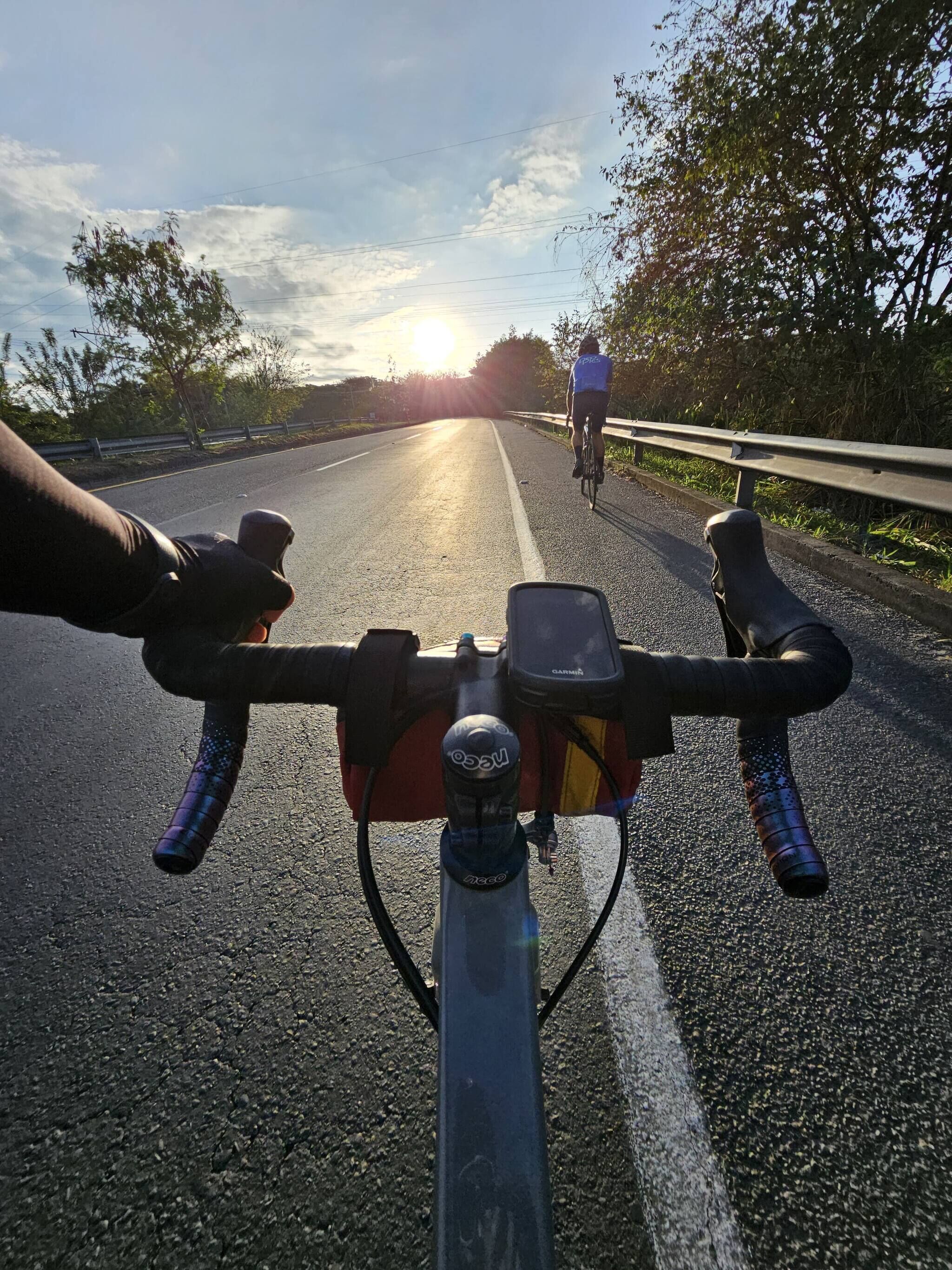 Manillar de bicicleta y carretera con un ciclista a lo lejos.