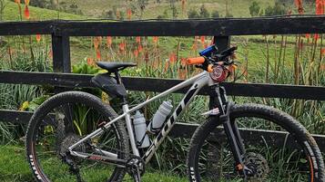Una mountain bike parcheggiata su un sentiero sterrato con una recinzione di legno e vista su dolci colline verdi sullo sfondo.