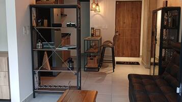 Una sala de estar con un sofá, una mesa de centro, una estantería y un comedor con una silla.