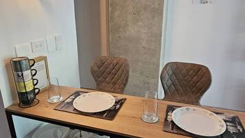 A dining area with a wooden table, two chairs, hanging pendant lights, and a wall-mounted electrical outlet.