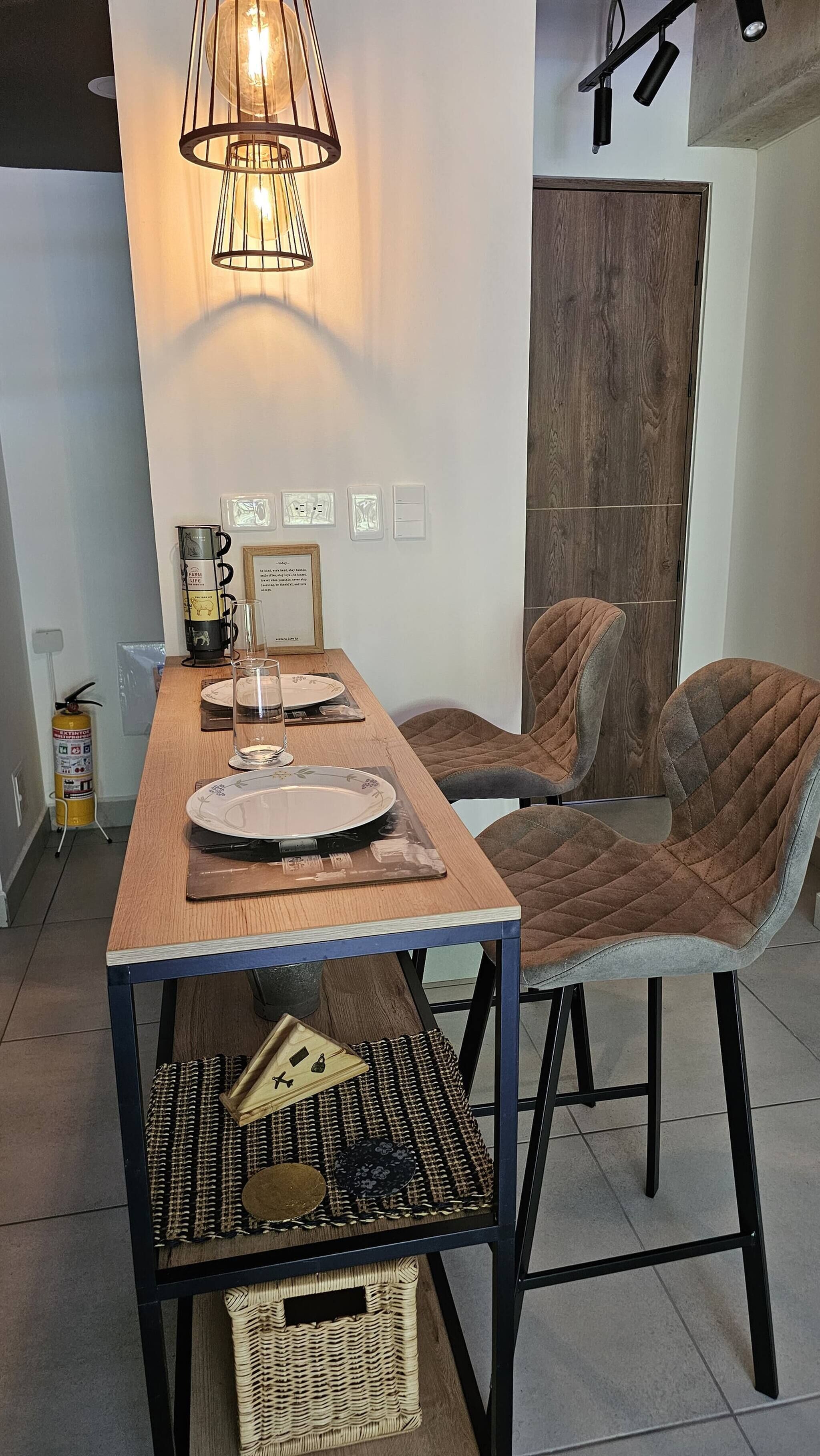 Zona pranzo con tavolo in legno, due sedie, lampadario a sospensione e una porta sullo sfondo.