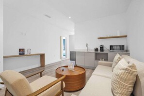 A modern living room with a sofa, chairs, a wooden coffee table, a kitchen area with a microwave, and a shelf with items. - Brickell Studio • View • 30min Miami Stadium (Miami)