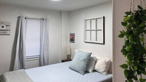 Ein Schlafzimmer mit Bett, einem Fenster mit Vorhängen, einem Wandbild, einer Nachttischlampe und einem Hinweisschild mit Zimmerverfügbarkeit.