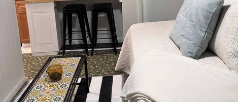 A compact hotel room with a kitchenette, a bed with pillows, a small table, and a striped rug.